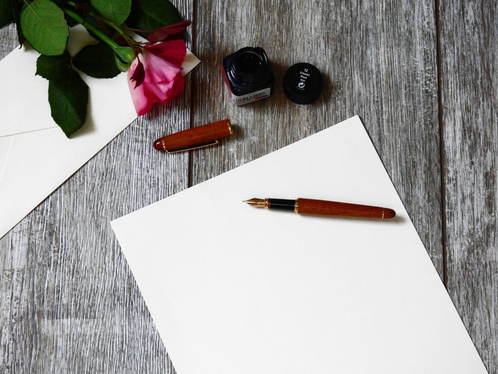 pexels-photo-356407-356407 Flat lay image of a rose, fountain pen, and paper on a rustic wooden table.